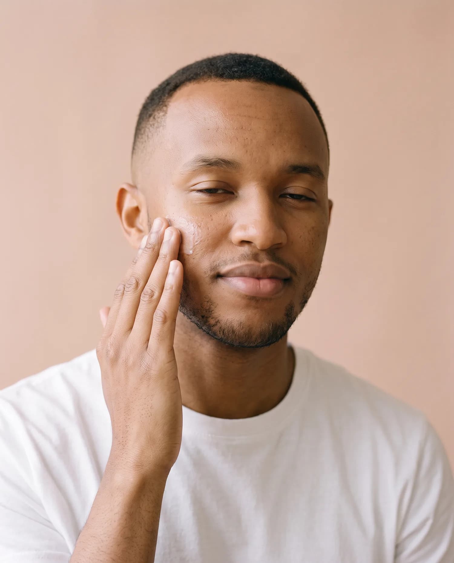 Campaign image: a young man pressing moisturiser into his cheek with his fingertips